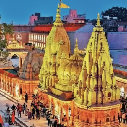 Aerial view of the illuminated Kashi Vishwanath Temple in Varanasi at dusk, showing its golden spires and numerous devotees gathered in the courtyard.