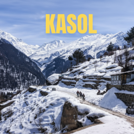 Panoramic winter landscape of Kasol, Himachal Pradesh, showing snow-covered mountain slopes, traditional village houses, a winding snowy road with people and a red car, and majestic snow-capped Himalayan peaks in the background, with 'KASOL' text overlay.