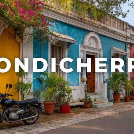 A beautiful and colorful street scene in the French Quarter of Pondicherry (Puducherry), showcasing brightly painted colonial houses in yellow, blue, and orange, lined with potted greenery. A black vintage motorcycle is parked on the cobblestone street with the text "PONDICHERRY" overlaying the image